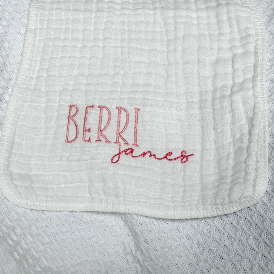 Personalized white baby burp cloth with embroidered first and middle names — "Berri" in pink block letters and "james" in darker pink script font. Custom baby gift on soft muslin fabric, perfect for newborns, baby showers, and keepsakes.