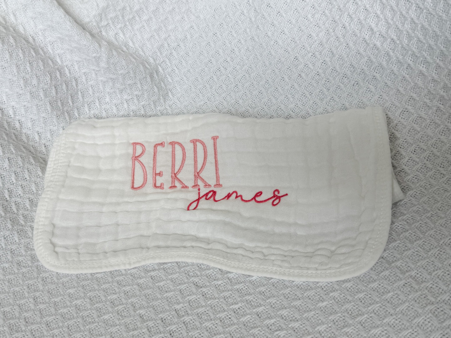 Personalized white baby burp cloth with embroidered first and middle names — "Berri" in pink block letters and "james" in darker pink script font. Custom baby gift on soft muslin fabric, perfect for newborns, baby showers, and keepsakes.